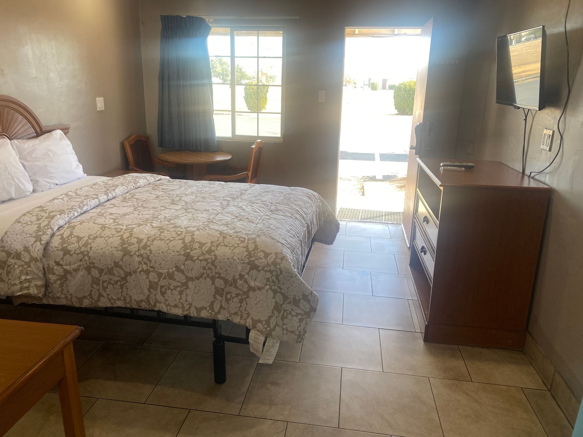 A hotel room with a bed , dresser , table and television.