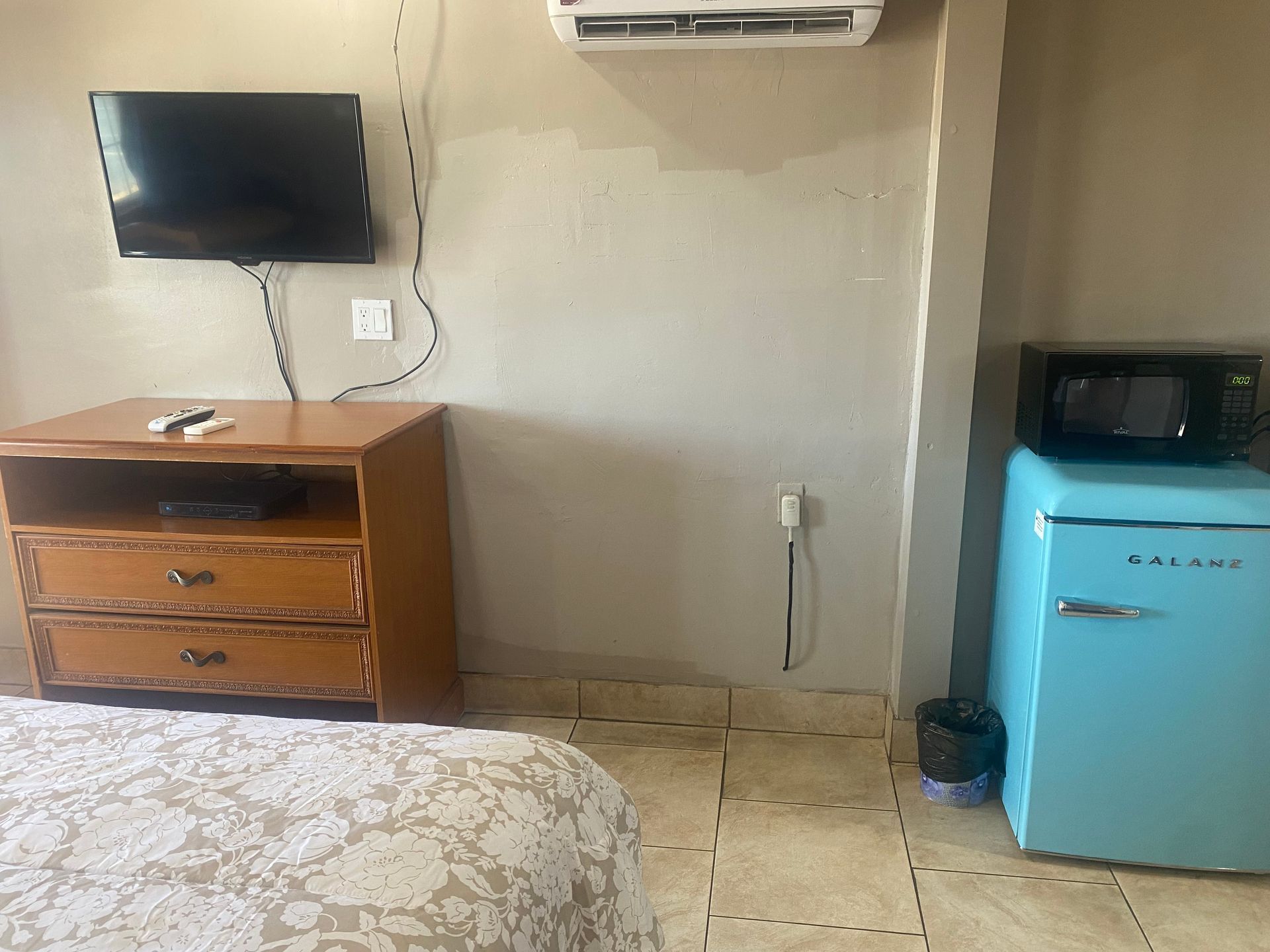 A bedroom with a bed , dresser , television , microwave and refrigerator.