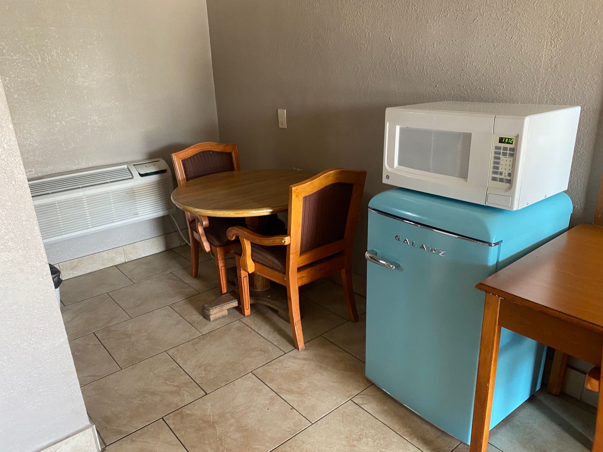 A room with a table, chairs, a microwave and a blue refrigerator.