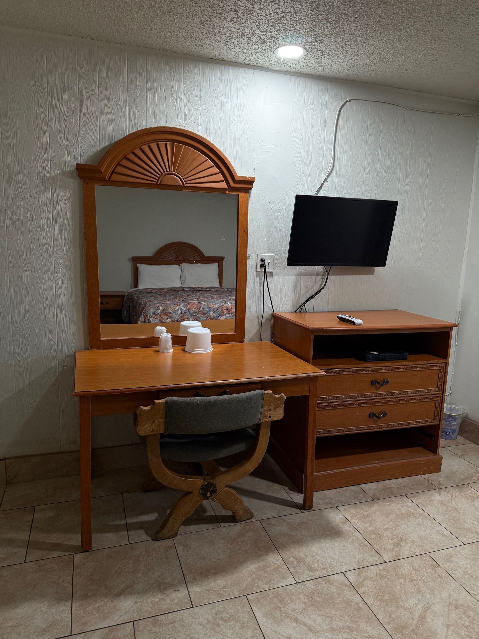 A hotel room with a desk , chair , mirror and television.