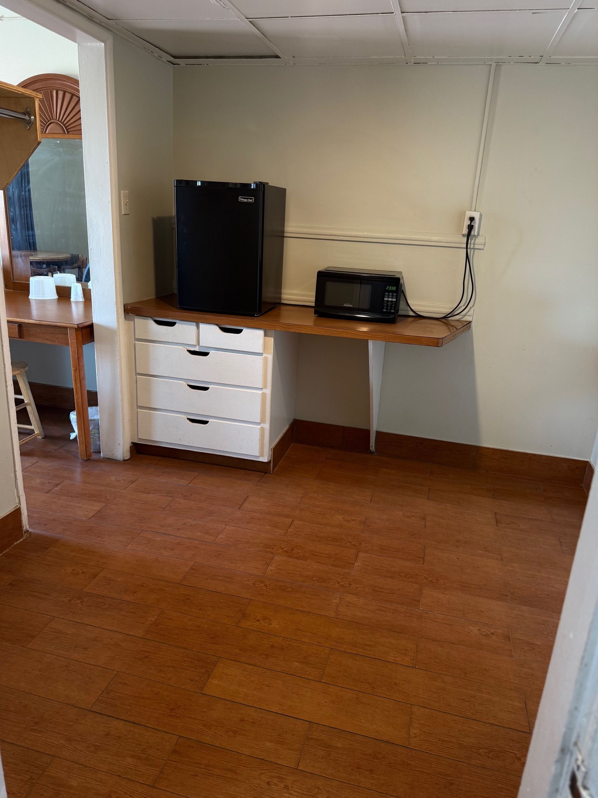 A room with a refrigerator , microwave and dresser