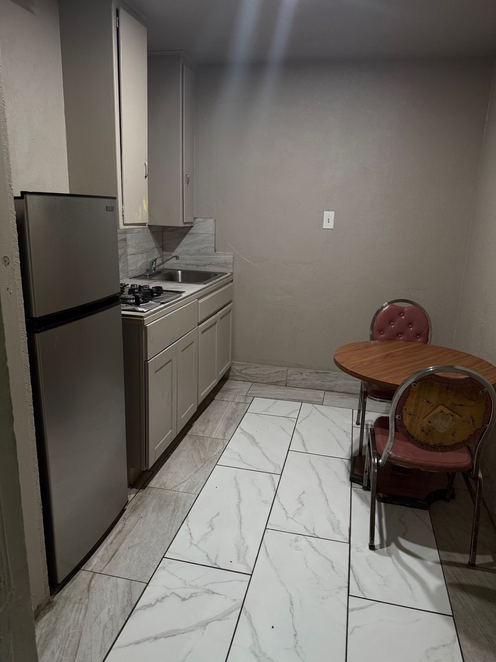 A kitchen with a refrigerator , sink , table and chairs.