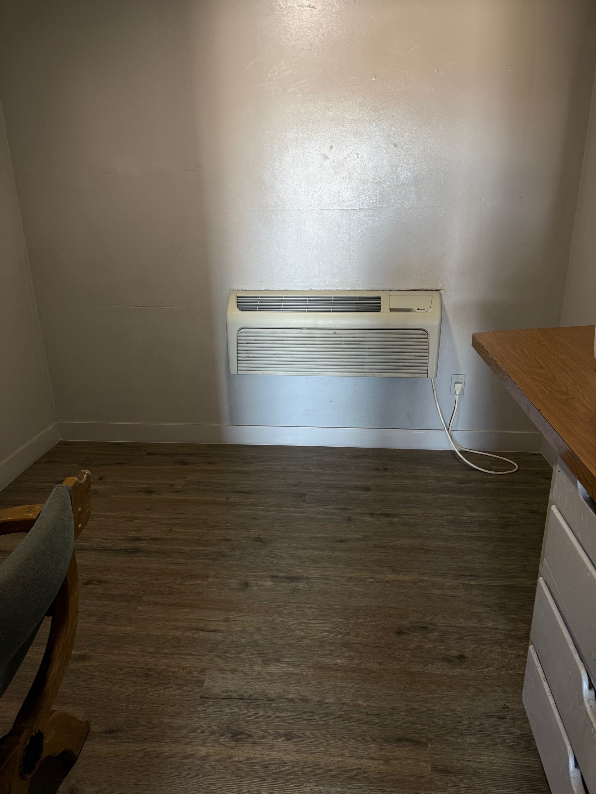 A room with a wall mounted air conditioner and a wooden floor.