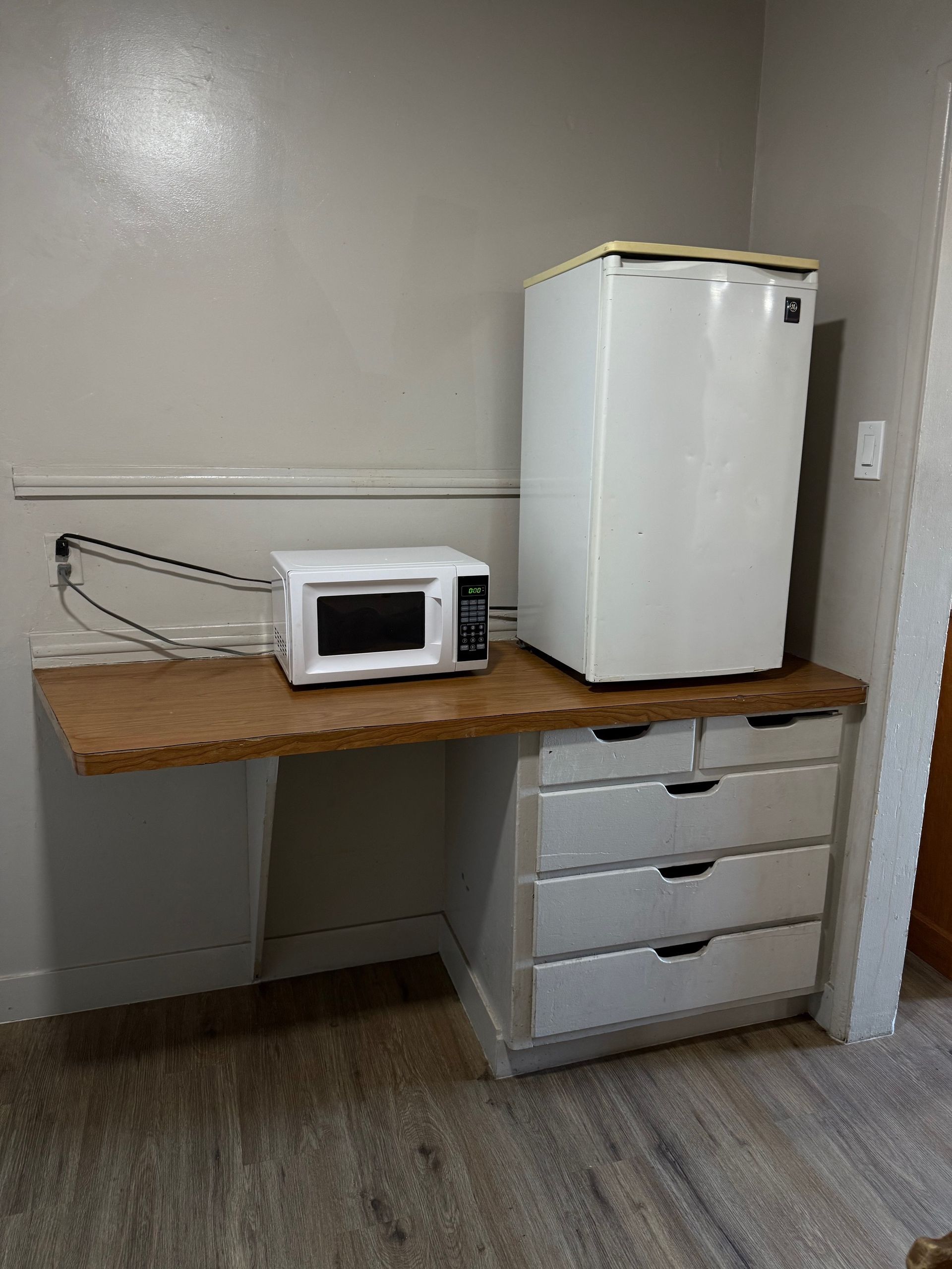 A microwave and a refrigerator are sitting on a wooden table.