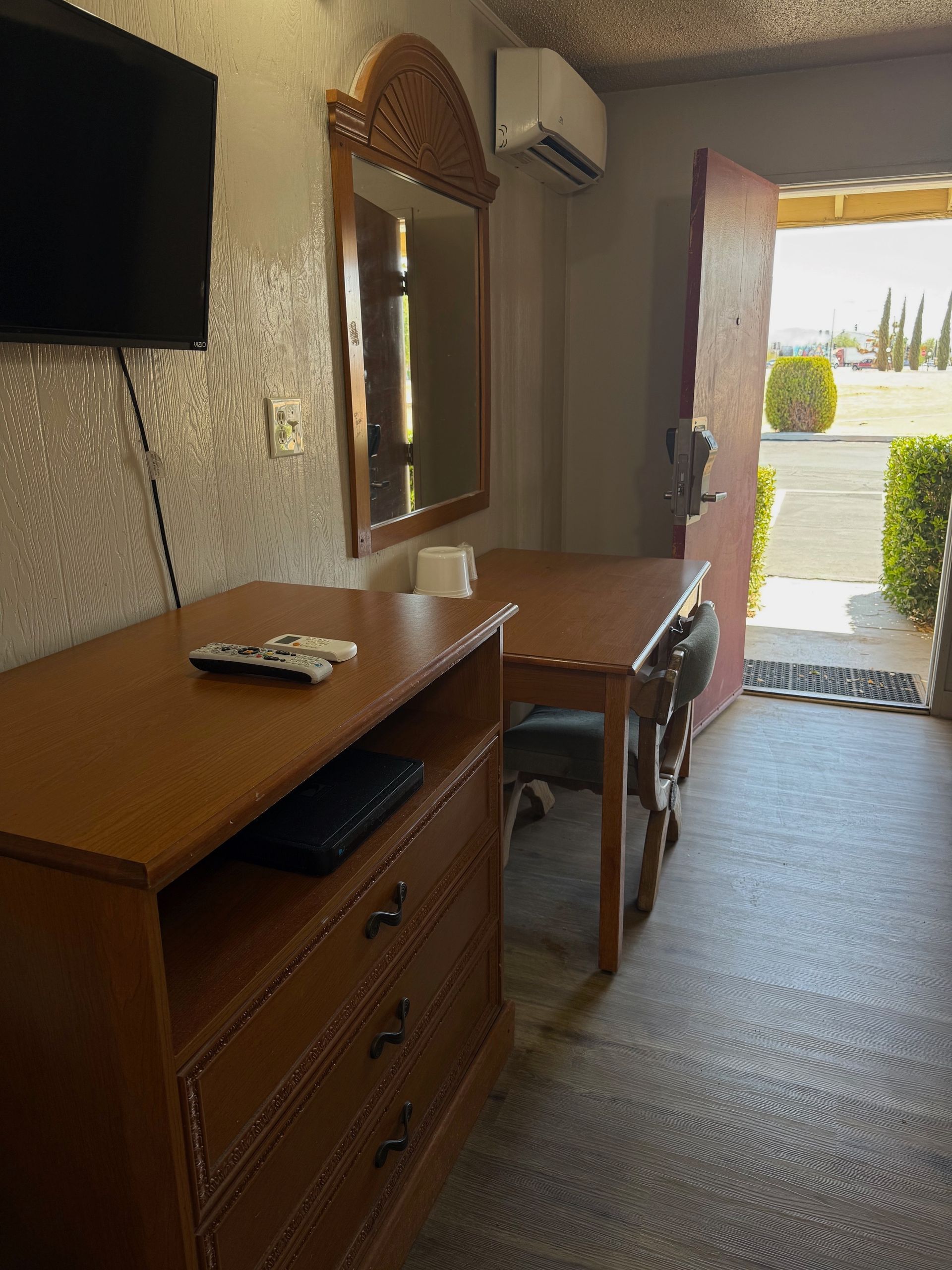 A hotel room with a table , dresser , television and mirror.