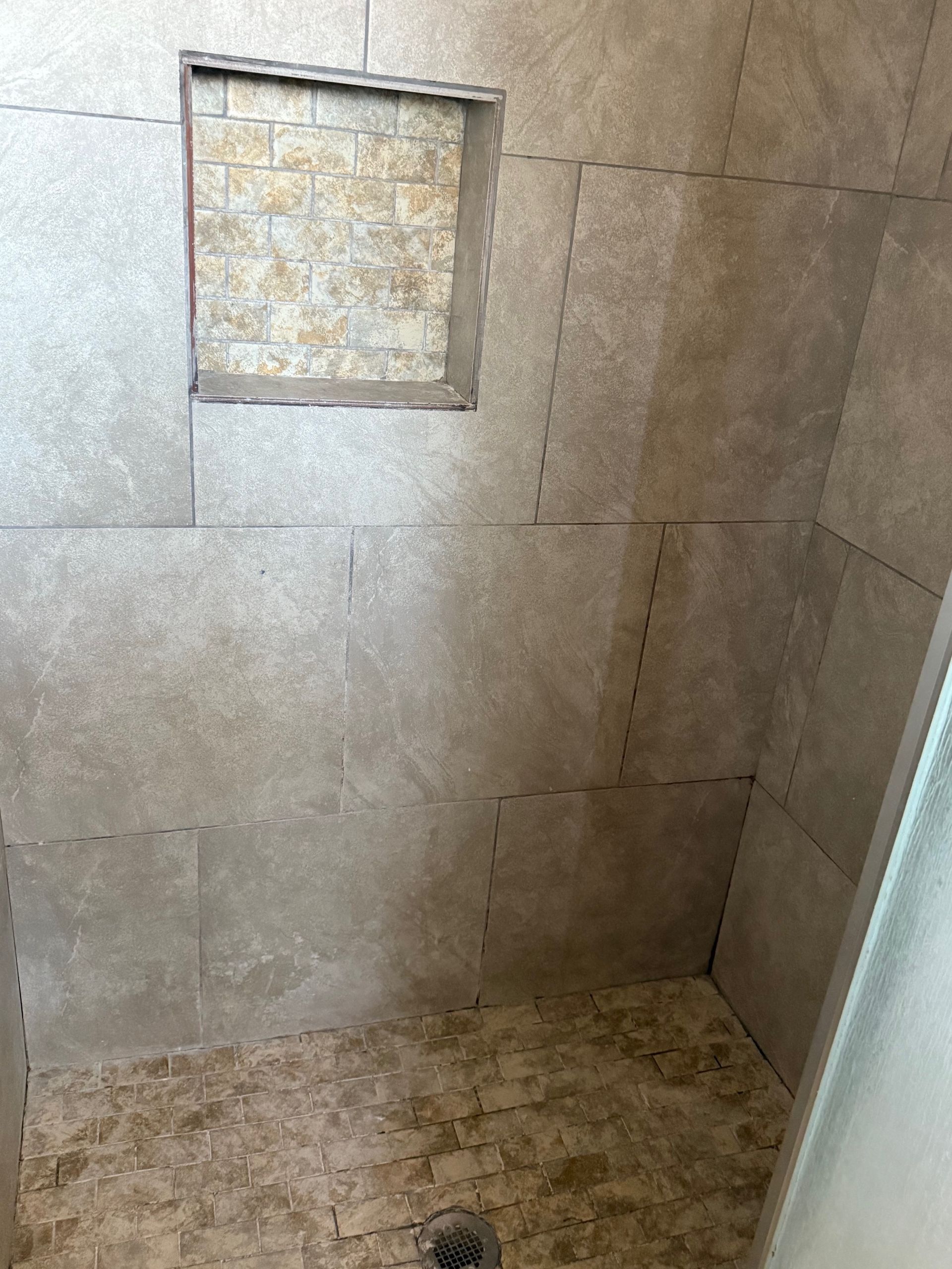 A shower stall with a drain and a niche in the wall.