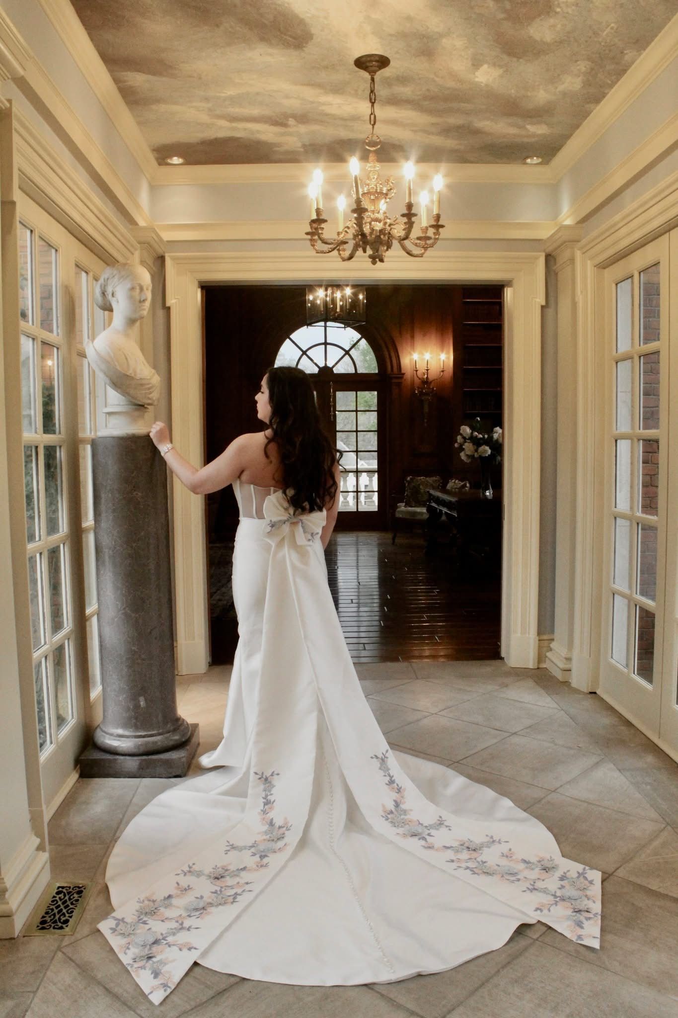 A woman in a wedding dress is standing in a hallway next to a statue.