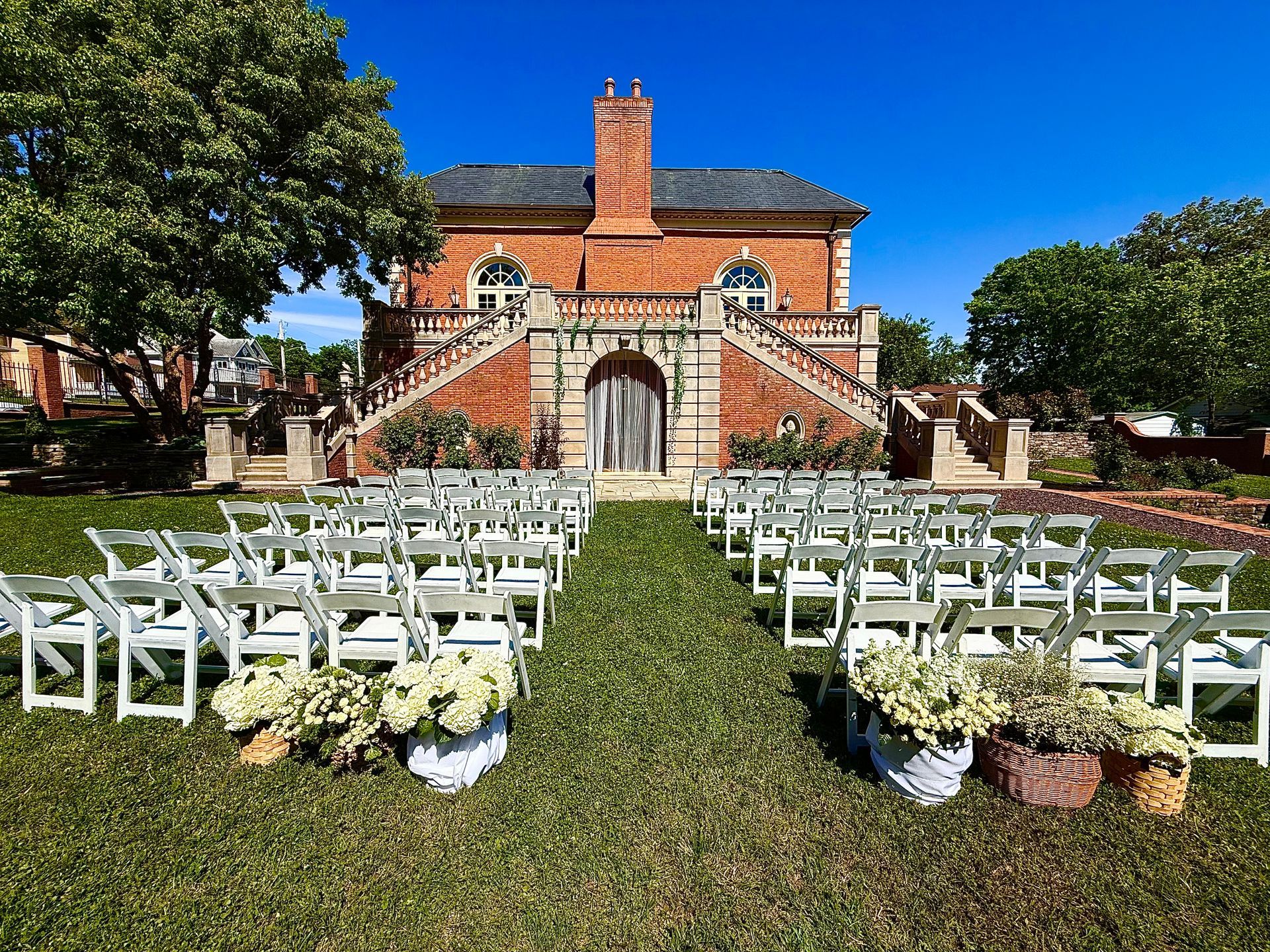 A row of white chairs are lined up in front of a large brick building.