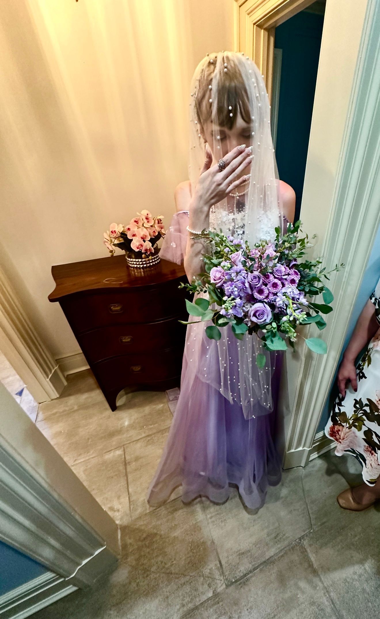 A woman in a purple dress is holding a bouquet of purple flowers.