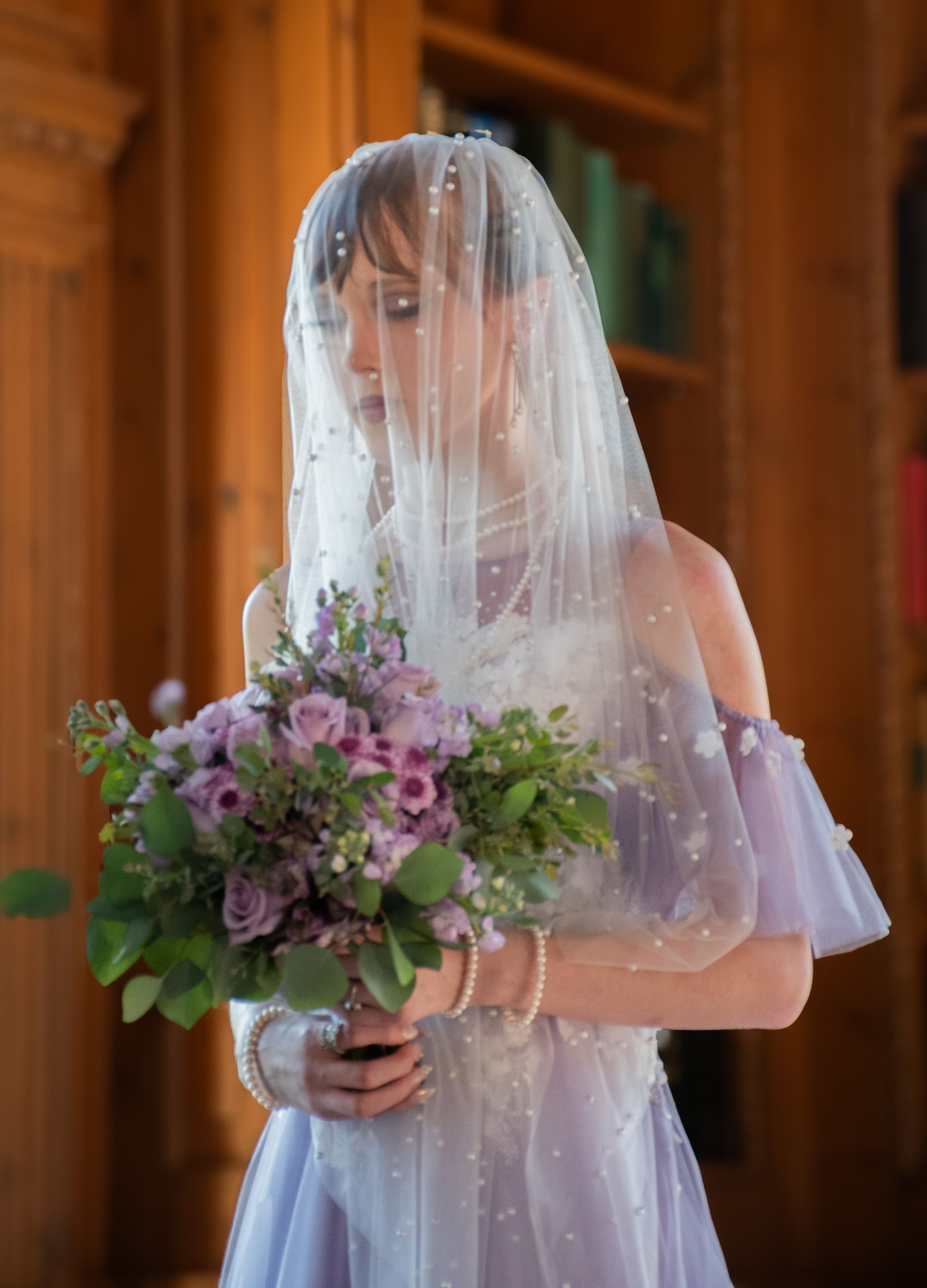 The bride is wearing a veil and holding a bouquet of purple flowers.