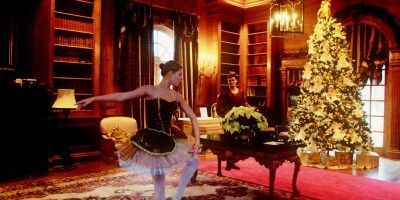 A ballerina is dancing in a room with a christmas tree in the background.