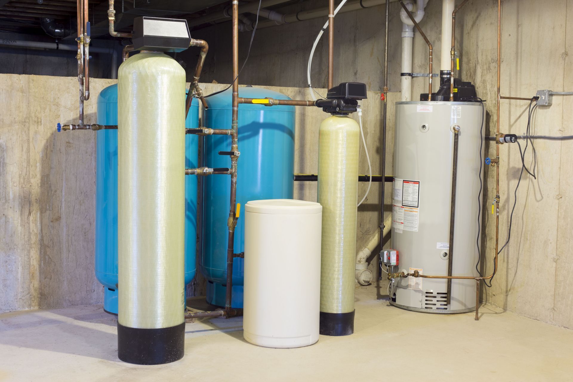 Basement water treatment system with tall white tanks and blue storage tanks against concrete walls