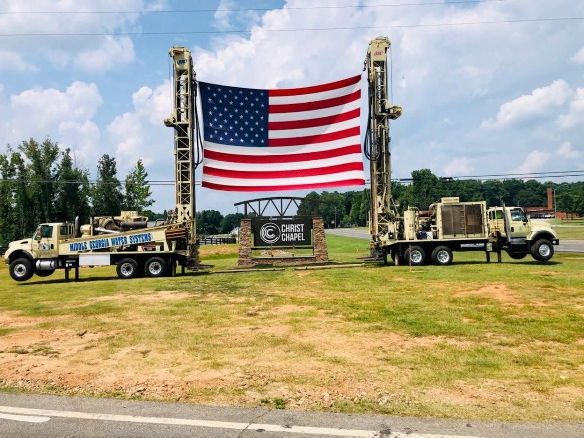 Two military trucks flank a giant American flag on display outdoors on a grassy field.