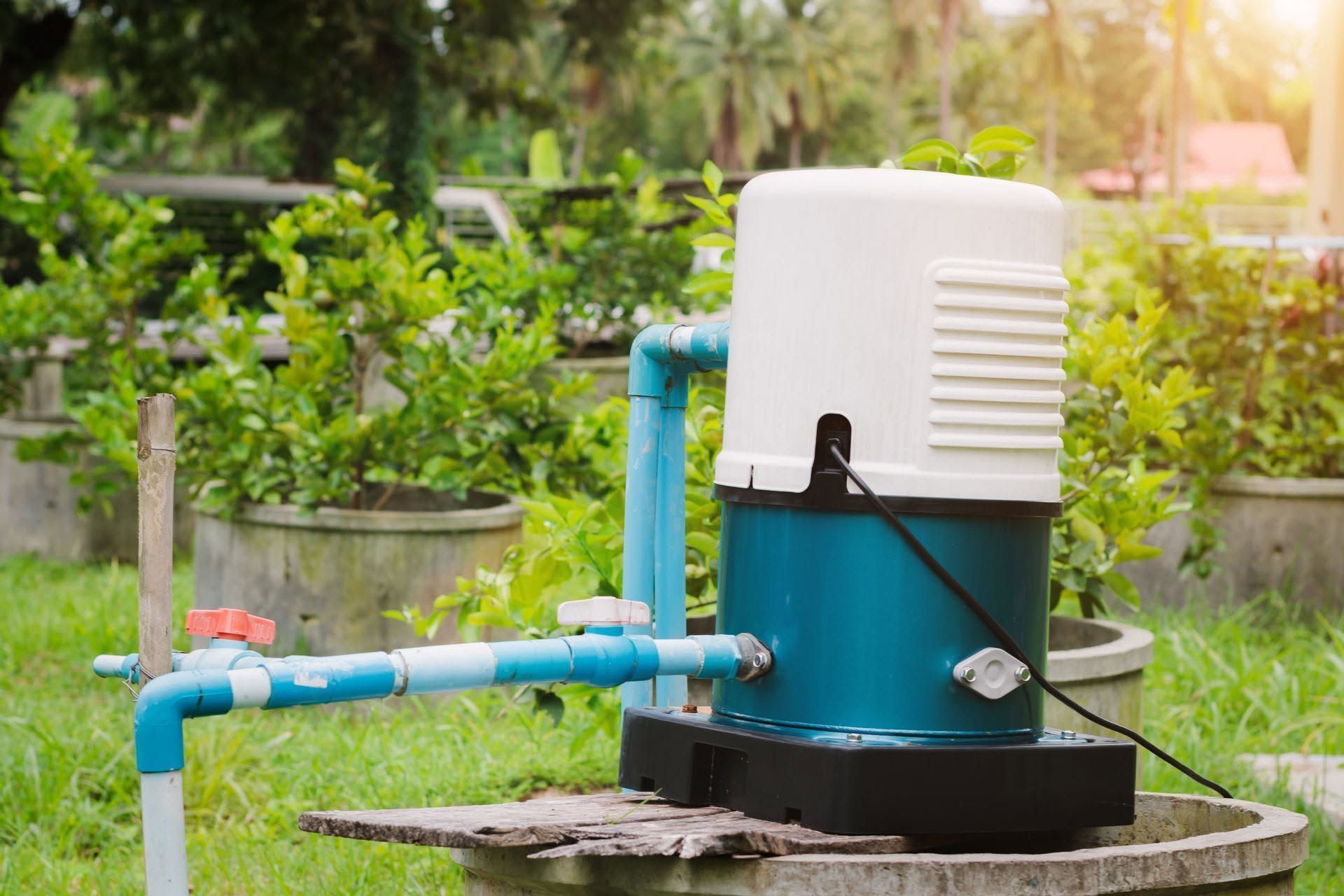Blue garden water pump with white top and pipes on a stone base in a lush outdoor setting