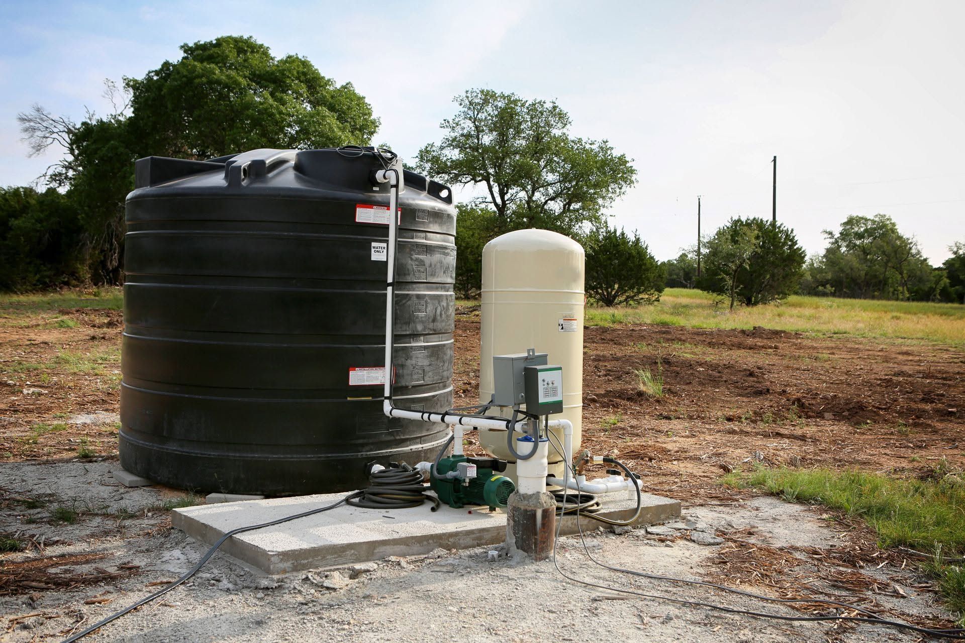 Two large water tanks and a pump setup on a gravel pad in a rural field