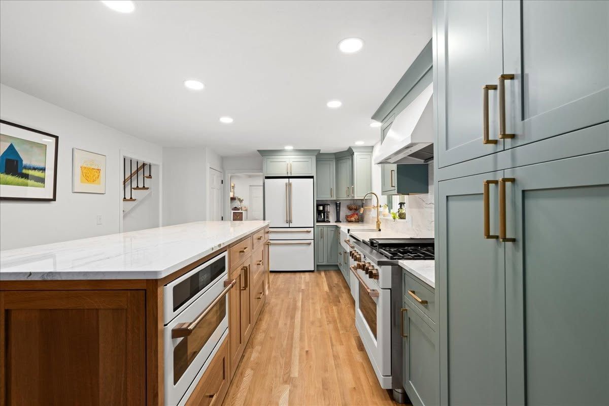 Modern kitchen with wood floors, white countertops, and gray cabinets, viewed from the center aisle