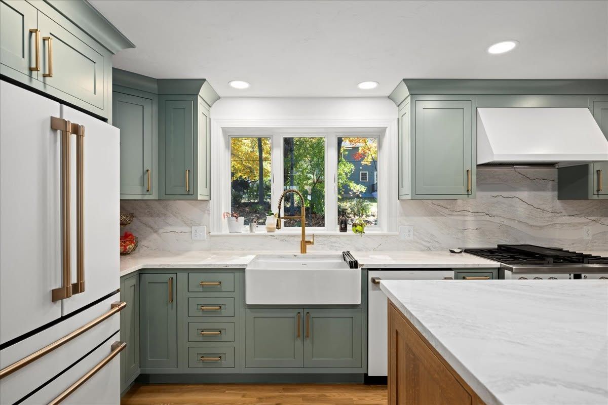 Bright modern kitchen with sage cabinets, white countertops, large window, and stainless steel appliances