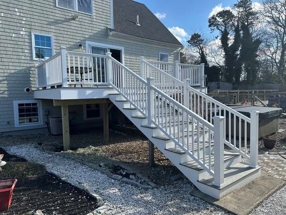 White wooden exterior staircase with railings leading to a raised deck on a house.