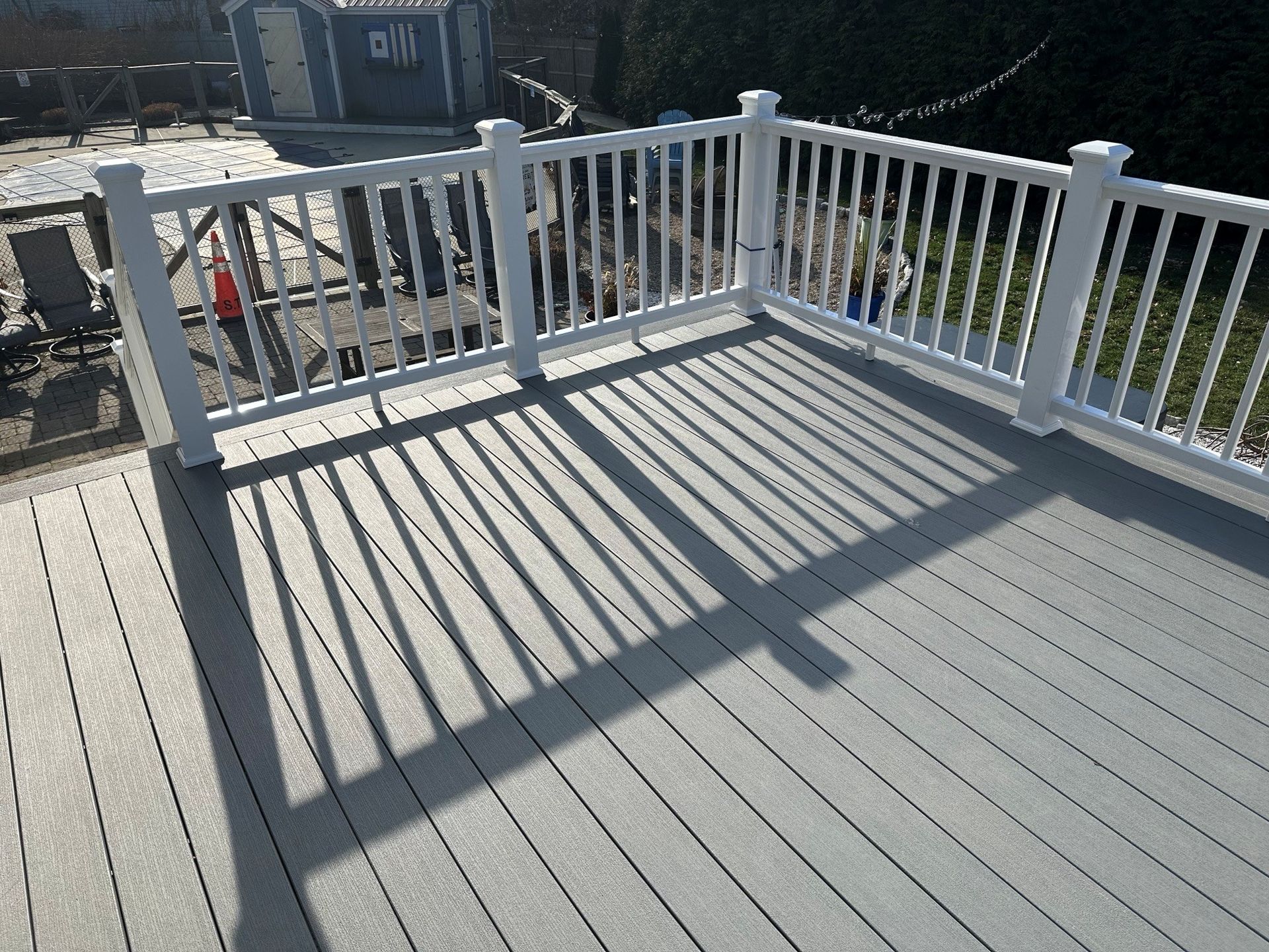 White-railed wooden deck in bright sunlight, casting long shadows across gray floorboards.