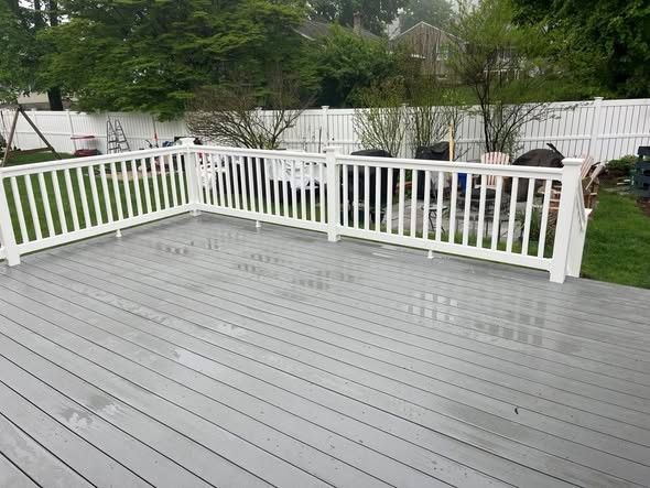 Gray wooden deck with white railing overlooking a backyard and trees