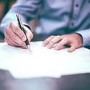 Person writing with a pen on white paper, close-up of hands and document.