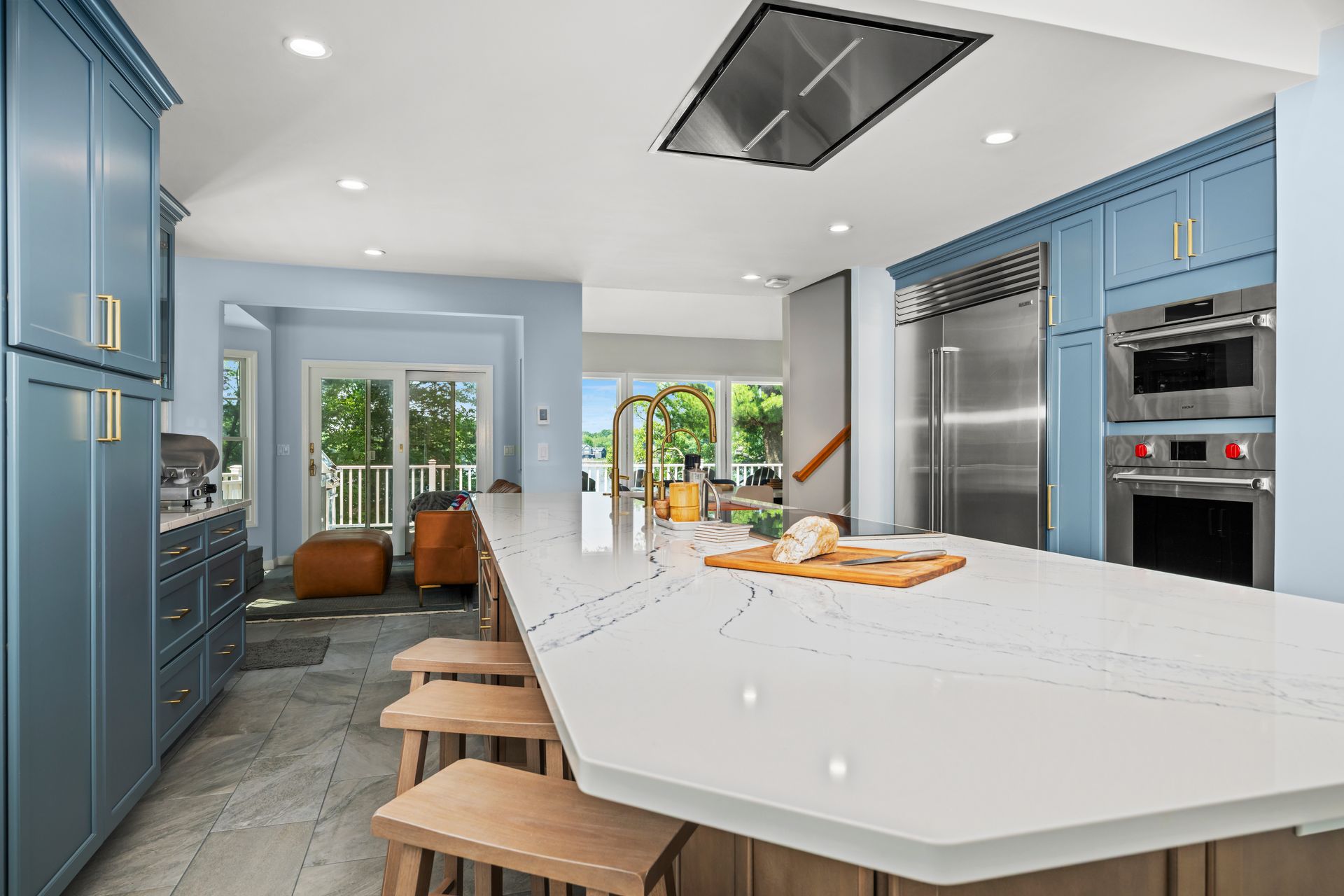 Modern blue kitchen with large white island, stools, built-in appliances, and bright sliding doors to patio