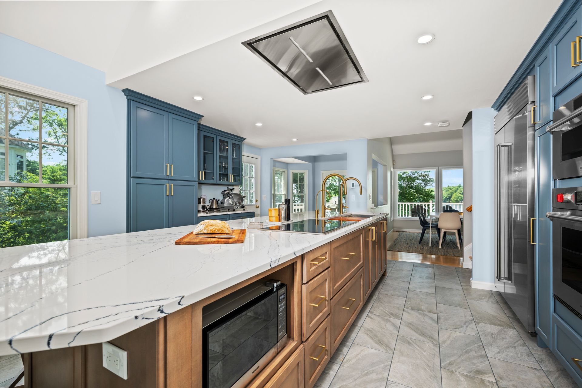 Bright modern kitchen with blue cabinets, marble island, and a windowed dining area