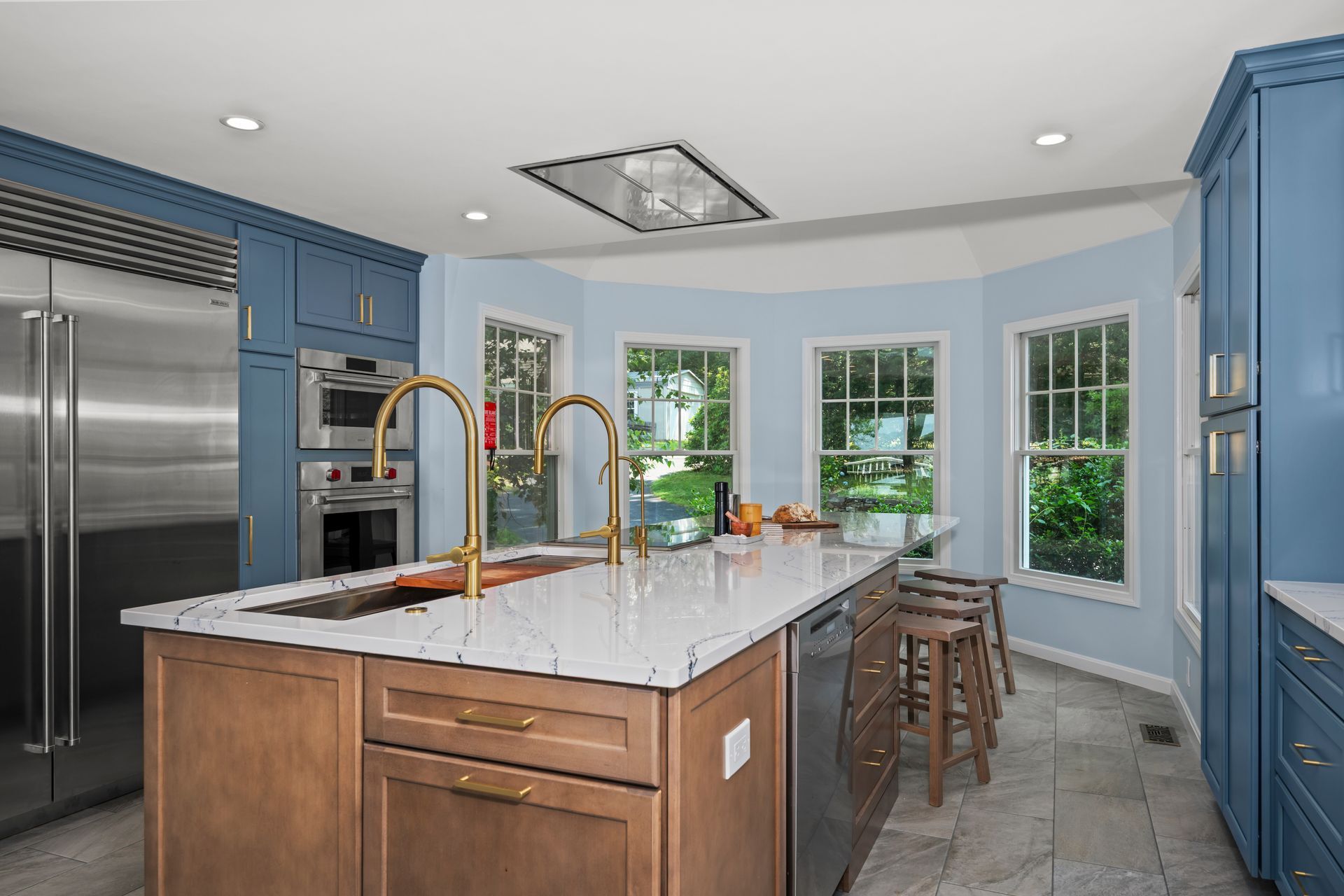 Modern kitchen with blue cabinets, marble island, stainless fridge, and large windows