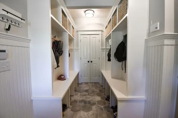 White hallway with built-in storage. Benches, hooks, and baskets line the walls. Door at the end.