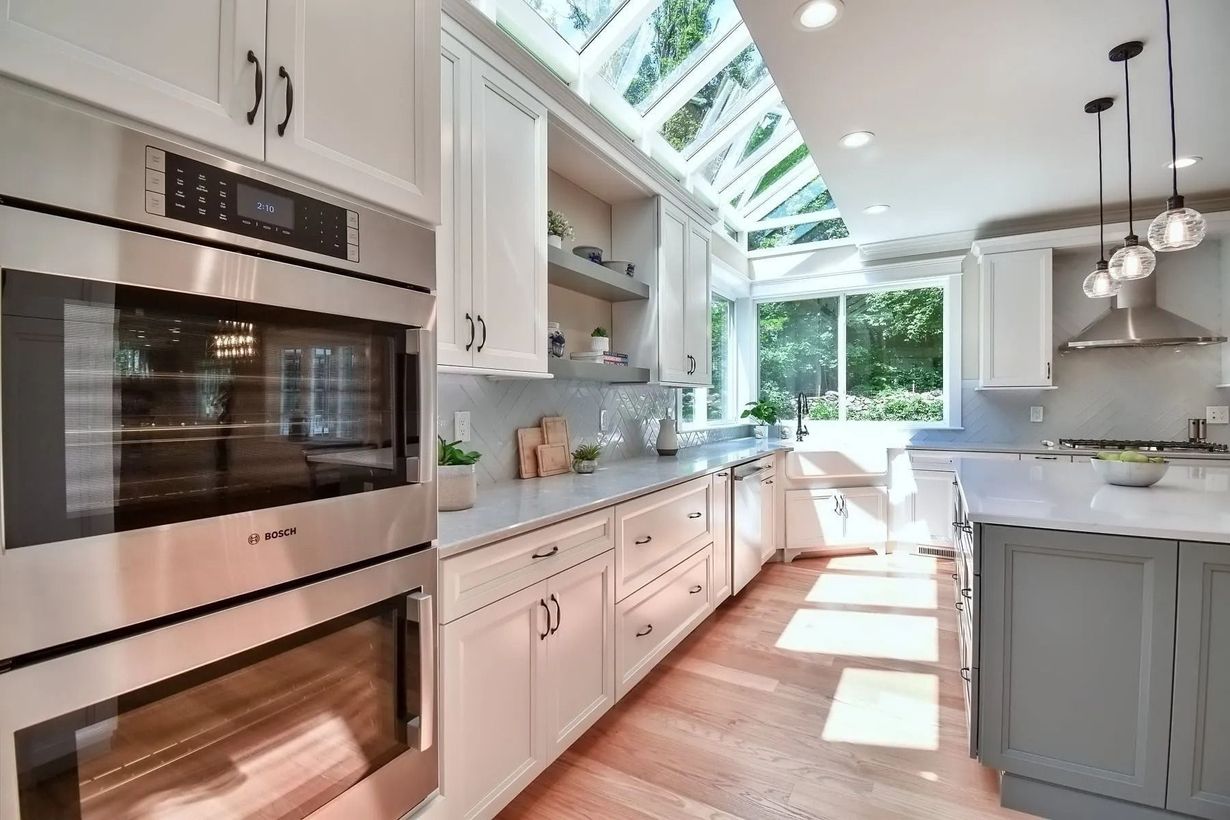 Modern kitchen with stainless steel oven, white cabinets, and a skylight; light wood floor.