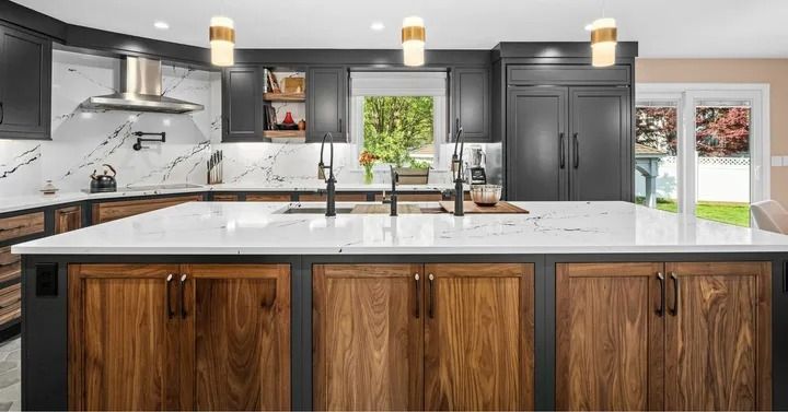 Modern kitchen with dark cabinetry, wood island, white countertops, and stainless steel appliances.