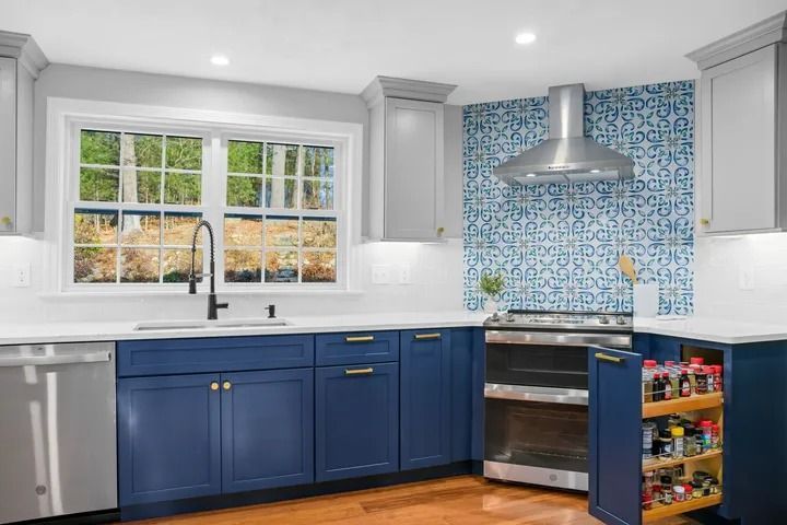 Modern kitchen with blue and gray cabinets, stainless steel appliances, and a mosaic backsplash.