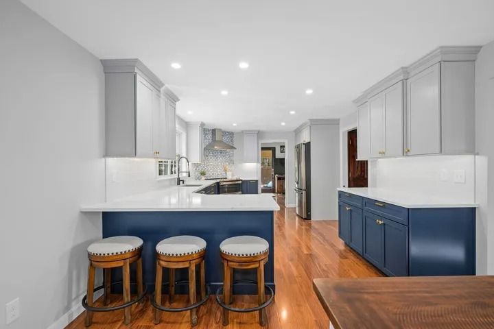 Kitchen with blue and gray cabinets, white countertops, and wood floors. Three bar stools at a blue island.