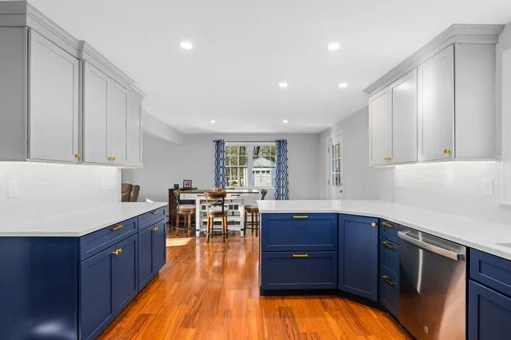 Modern kitchen with blue and white cabinets, wood floors, and white countertops.