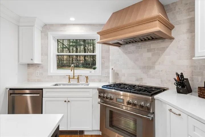 Kitchen with white cabinets, stainless steel appliances, and wood range hood.