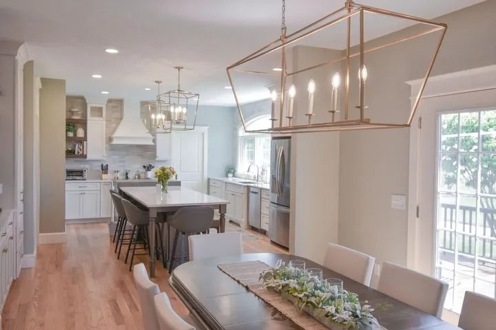 Spacious kitchen with island, dining table, and modern gold light fixtures. Bright, light wood floors.