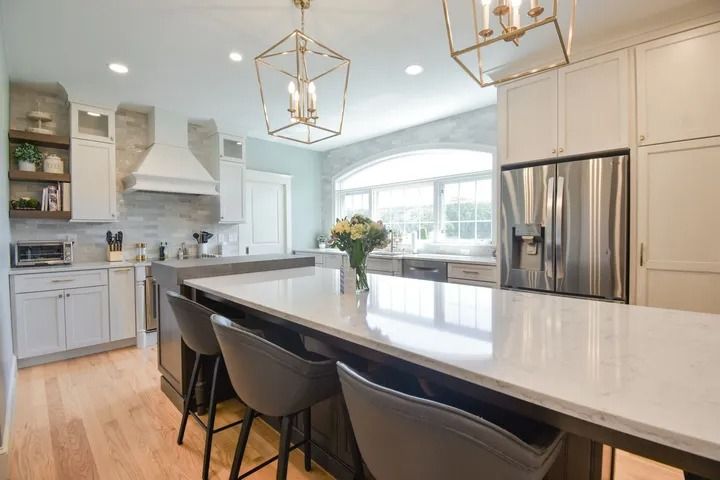 Modern kitchen with white cabinets, island with stools, and stainless steel refrigerator.