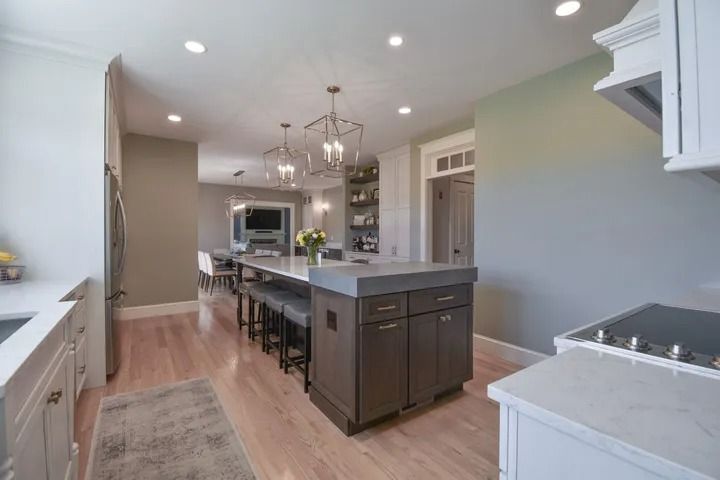Modern kitchen with an island, dark cabinets, pendant lights, and wooden floors.
