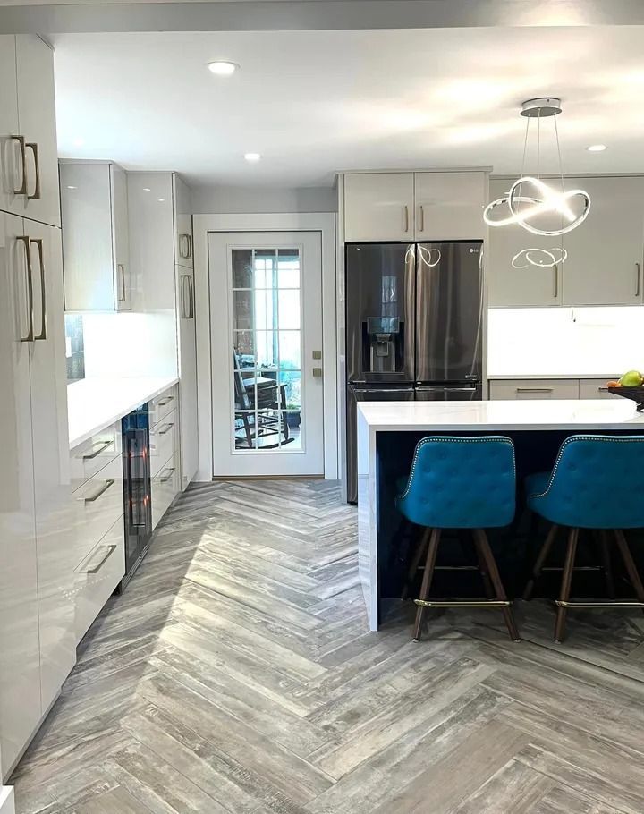 Modern kitchen with white cabinets, dark island with teal stools, and herringbone floor.