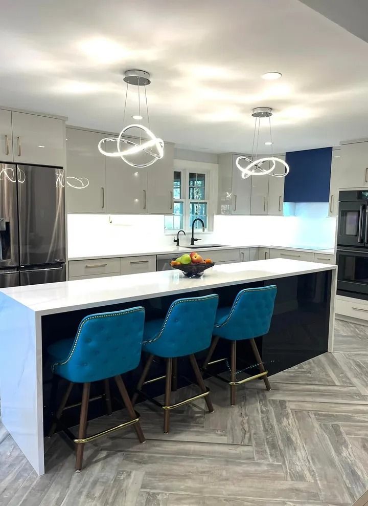 Modern kitchen with white countertops, blue bar stools, and pendant lights.