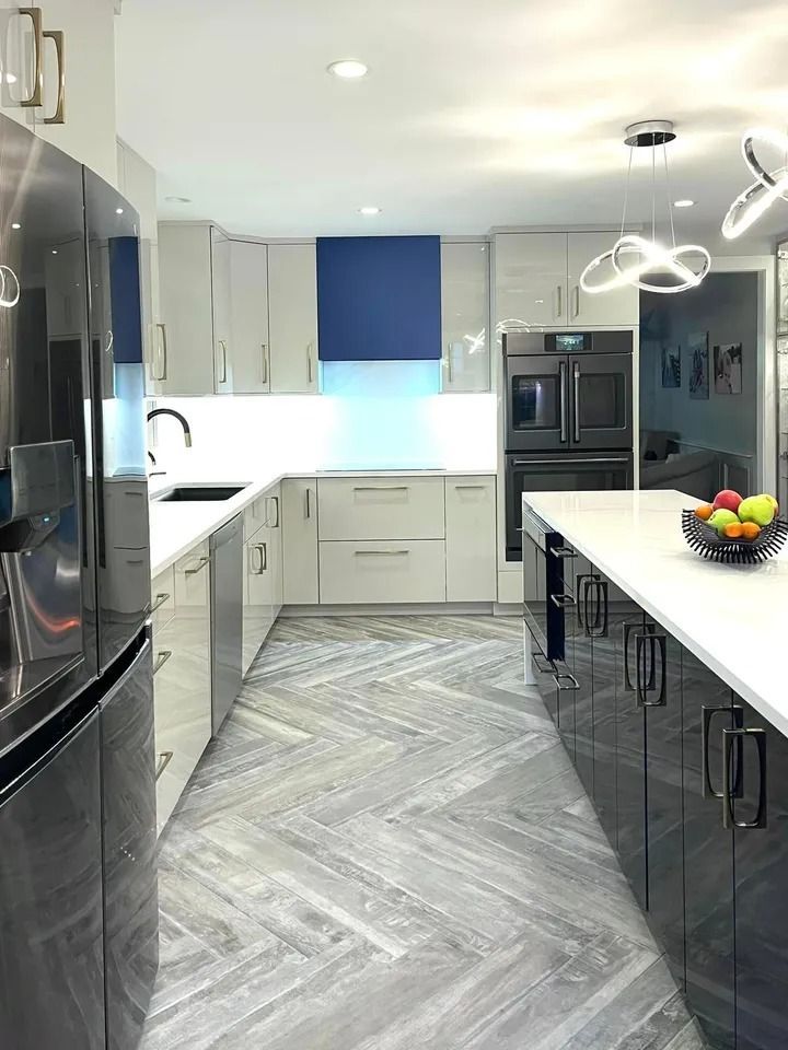 Modern kitchen with glossy gray cabinets, herringbone floor, blue range hood, and a white countertop island.