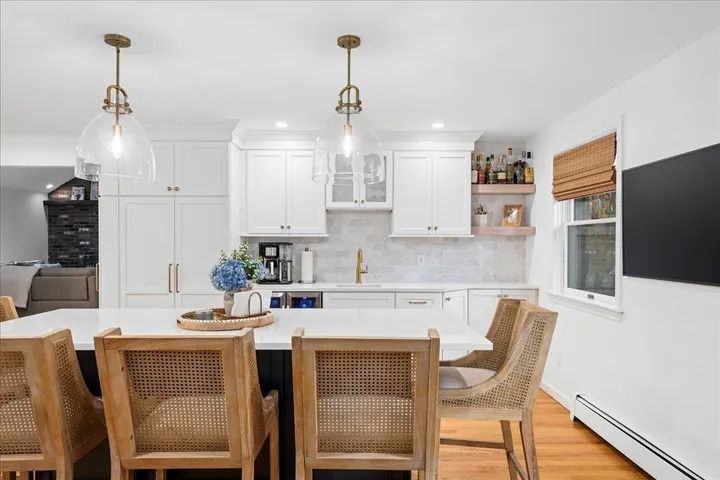 Kitchen with white cabinetry, large island, pendant lights, and rattan chairs.