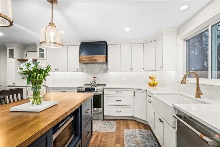 Modern kitchen with white cabinets, wood island, stainless steel appliances, and brass faucet.