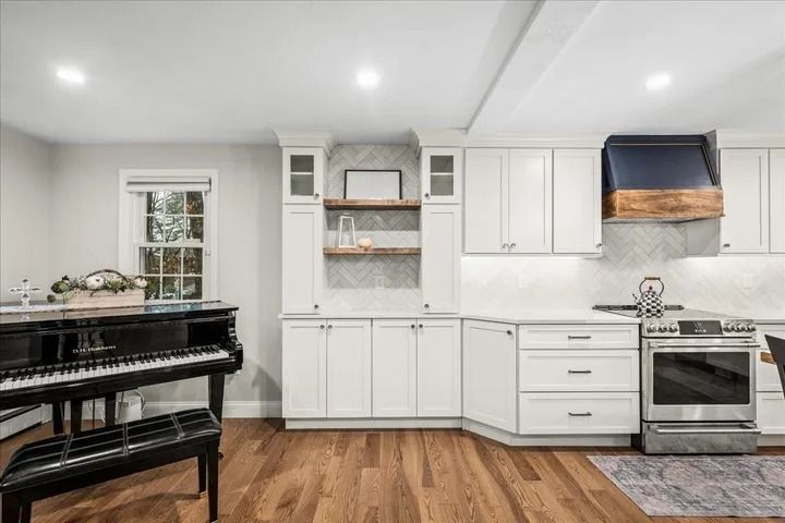 White kitchen with hardwood floors, piano, and stainless steel appliances.