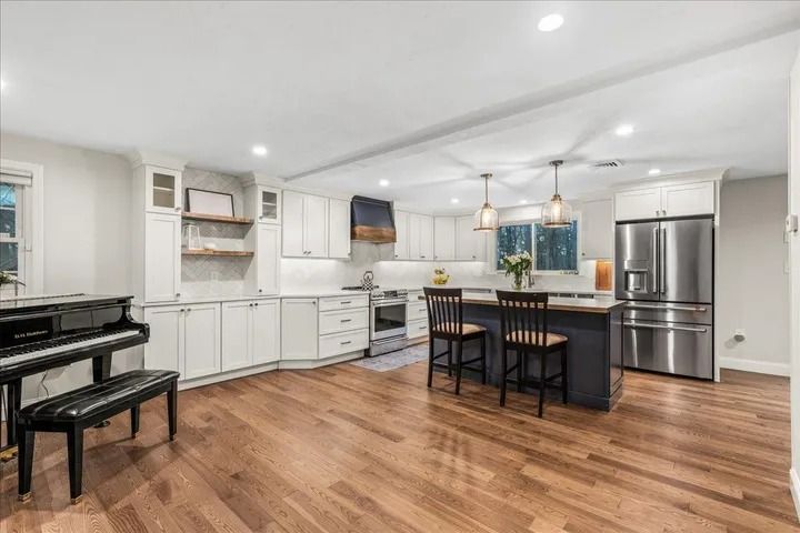Spacious kitchen with wood floors, white cabinets, stainless steel appliances, and a piano.