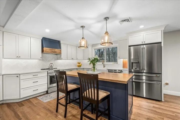 Modern kitchen with white cabinets, blue island, stainless steel appliances, and wood flooring.