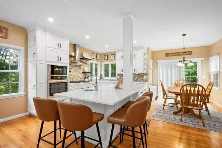 Spacious white kitchen with island seating, hardwood floors, and a dining area.