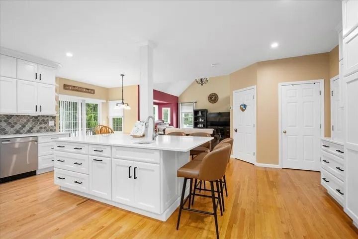 Modern kitchen with white cabinets, island with stools, and hardwood floors.