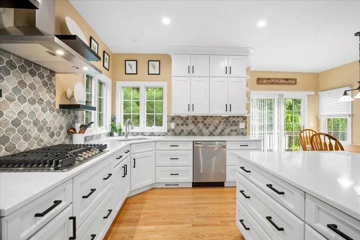 White kitchen with light wood floors, white cabinets, stainless steel appliances, and patterned backsplash.
