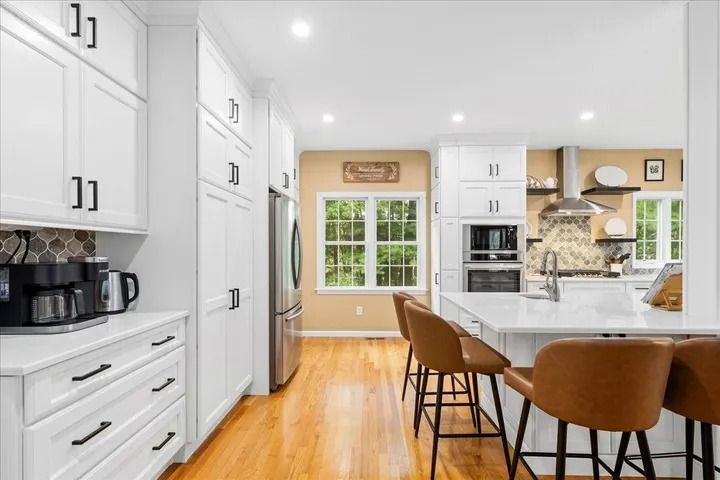 Bright white kitchen with stainless steel appliances, white cabinets, and a kitchen island with brown bar stools.